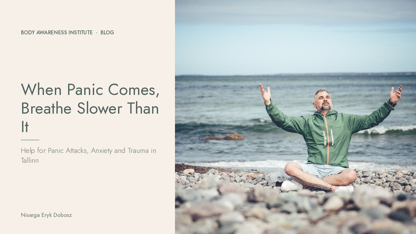 Nisarga Eryk Dobosz sitting cross-legged on a rocky Estonian shore by the sea, arms open, breathing calmly